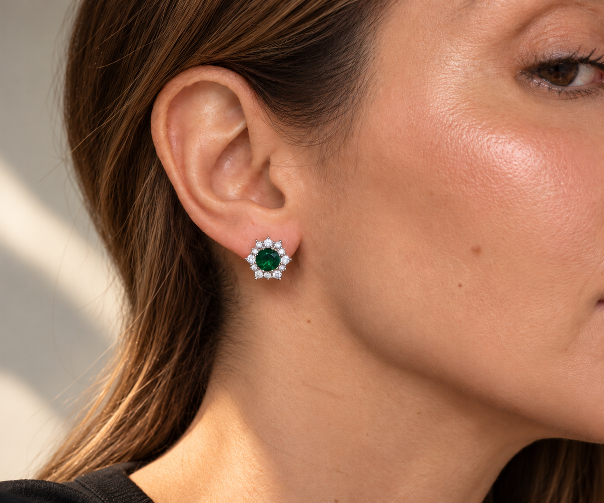 Modelo usando un arete Sary con piedra redonda verde y contorno floral de piedras transparentes.