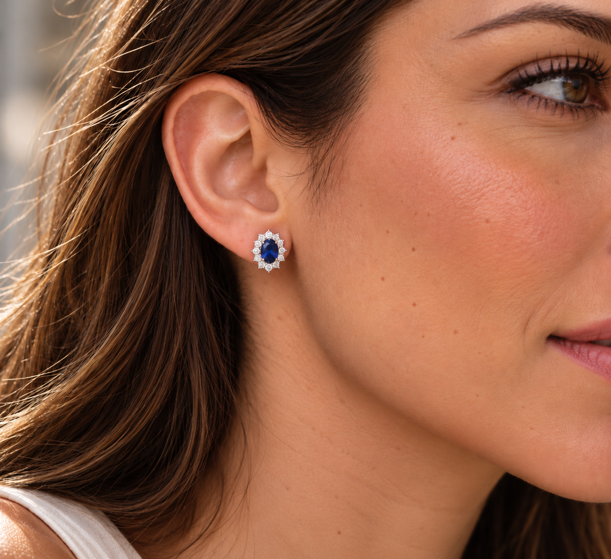 Modelo usando un arete Aya Azul con piedra ovalada azul y contorno de piedras transparentes.