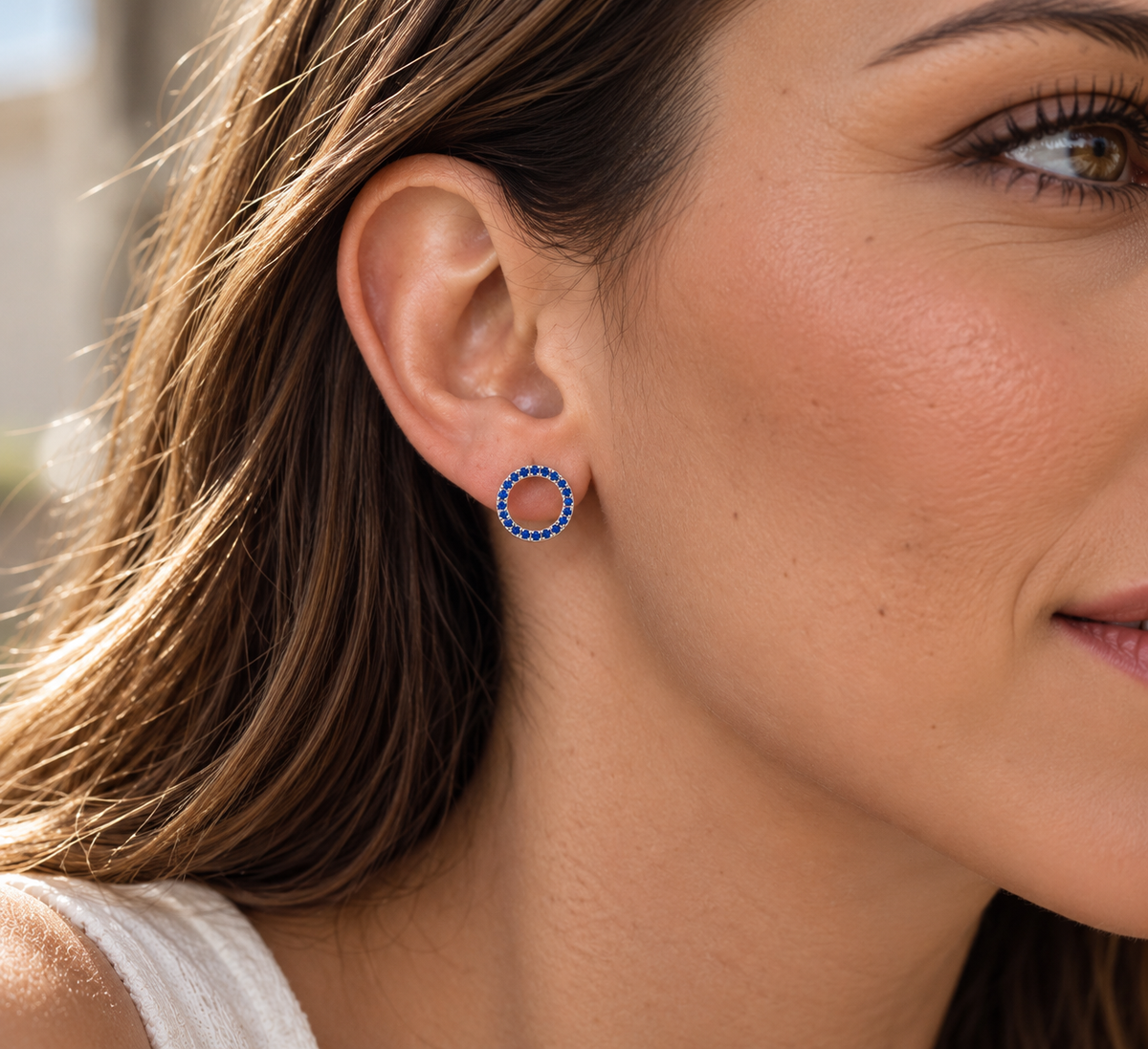 Modelo usando un arete Mona Azul de diseño circular con centro abierto y pequeñas piedras azules.