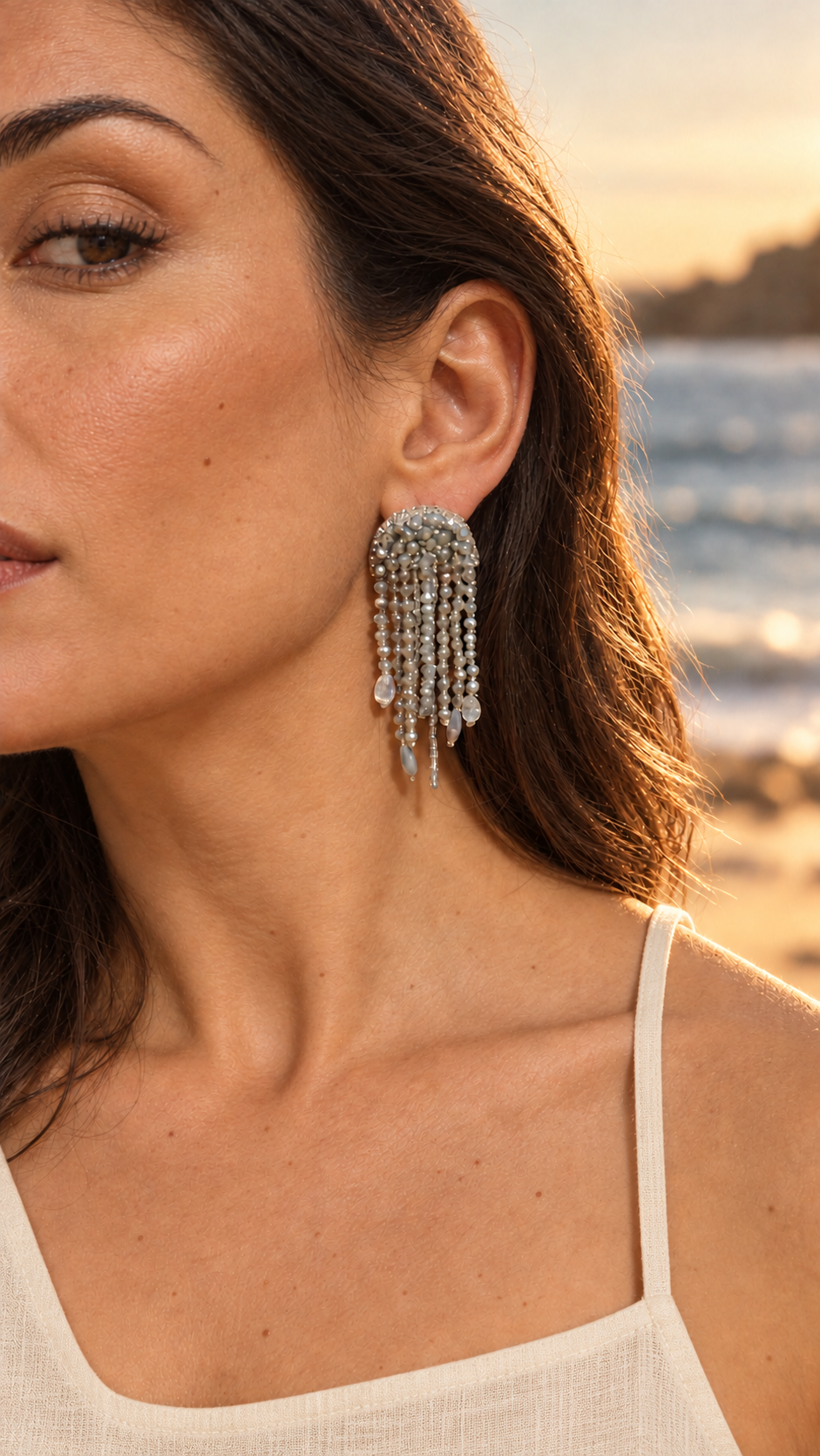 Modelo con un arete Medusa plateado de cuentas y colgantes en forma de gota junto al mar.
