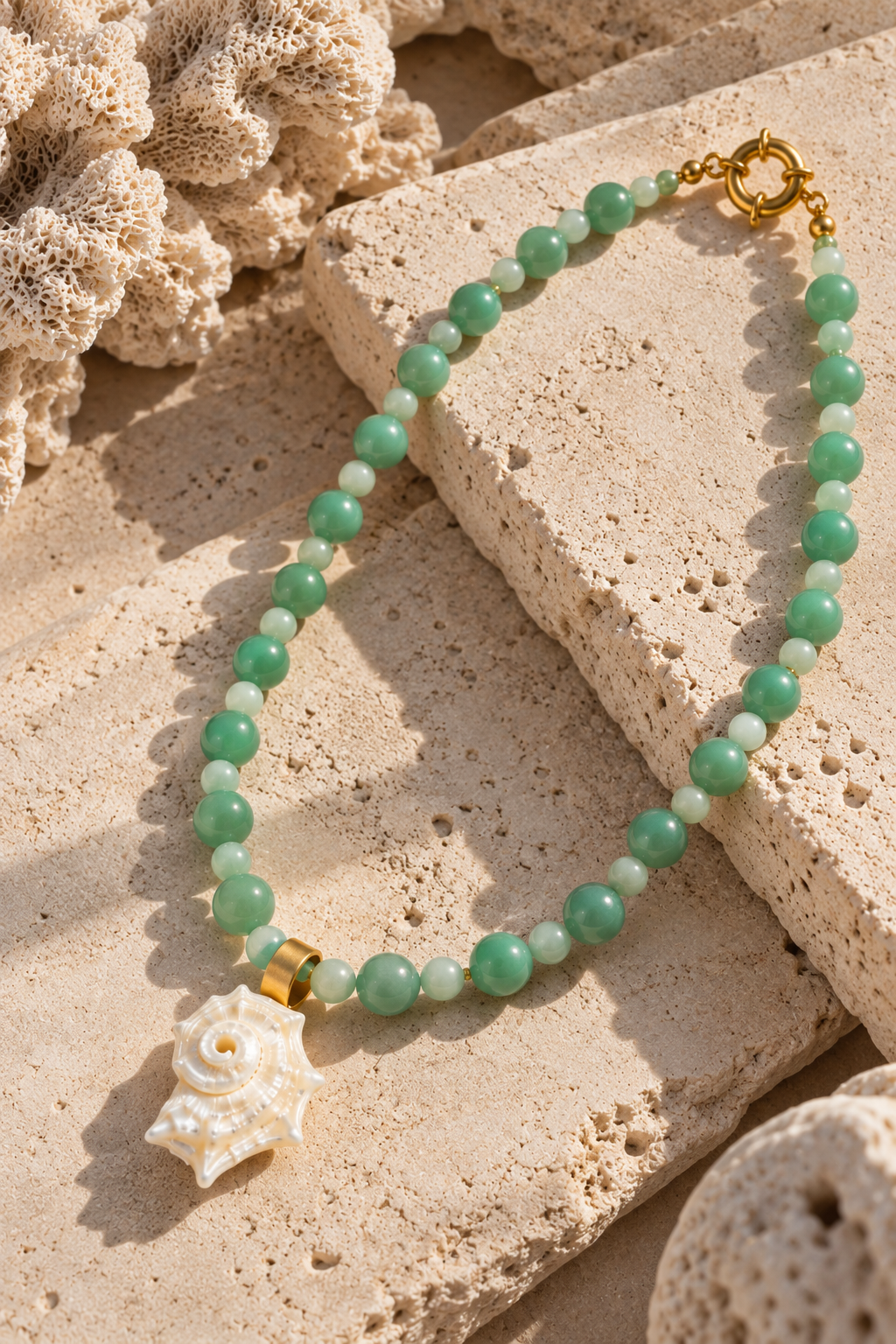 Collar Caracol de aventurina verde con dije de nácar y broche dorado sobre piedra beige.