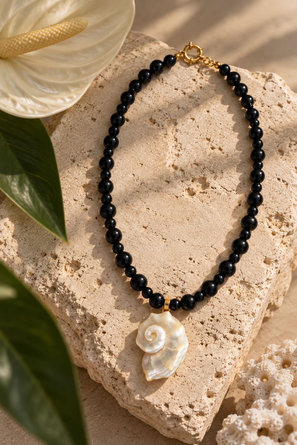 Collar Caracol de ónix negro con dije de nácar sobre piedra beige, junto a una flor blanca.