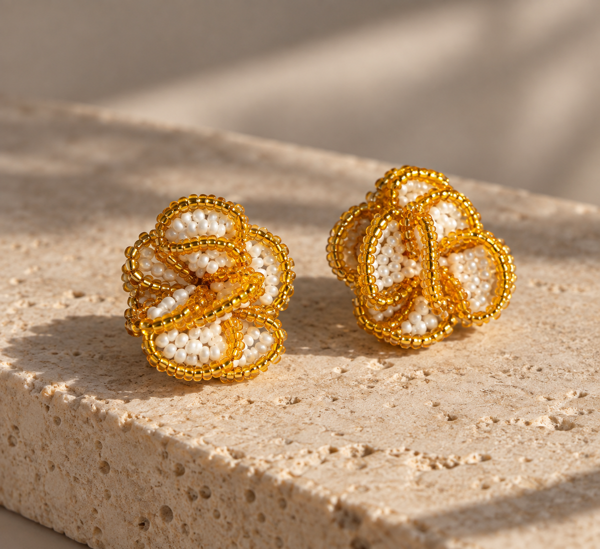 Par de aretes Crisantemo dorados de SALÁ, con pétalos de cuentas blancas sobre una base de piedra beige.