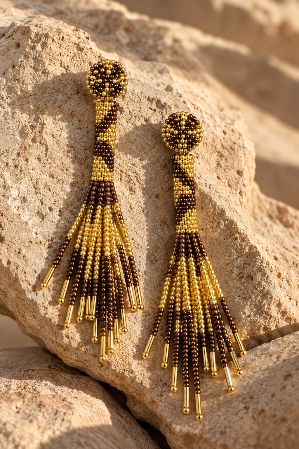 Aretes Cascada dorados con mostacillas color bronce y flecos largos sobre una piedra.