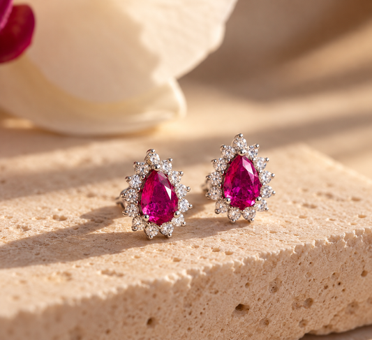 Aretes Coral Fucsia con piedras en forma de gota y contorno de piedras transparentes, sobre piedra beige.