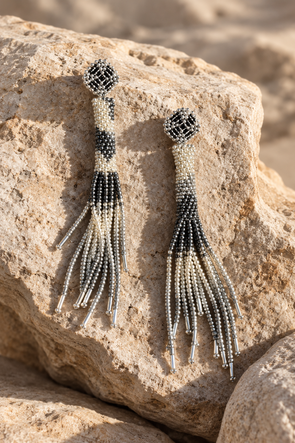 Aretes Cascada plateados con mostacillas negras y flecos largos sobre una piedra.