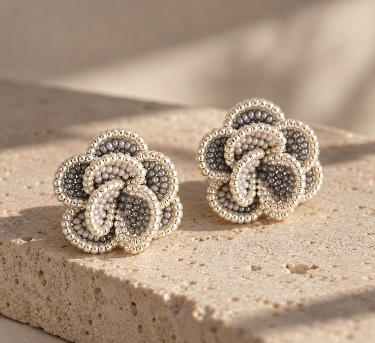 Par de aretes Crisantemo plateados de SALÁ, con pétalos de cuentas grises y blancas sobre piedra beige.