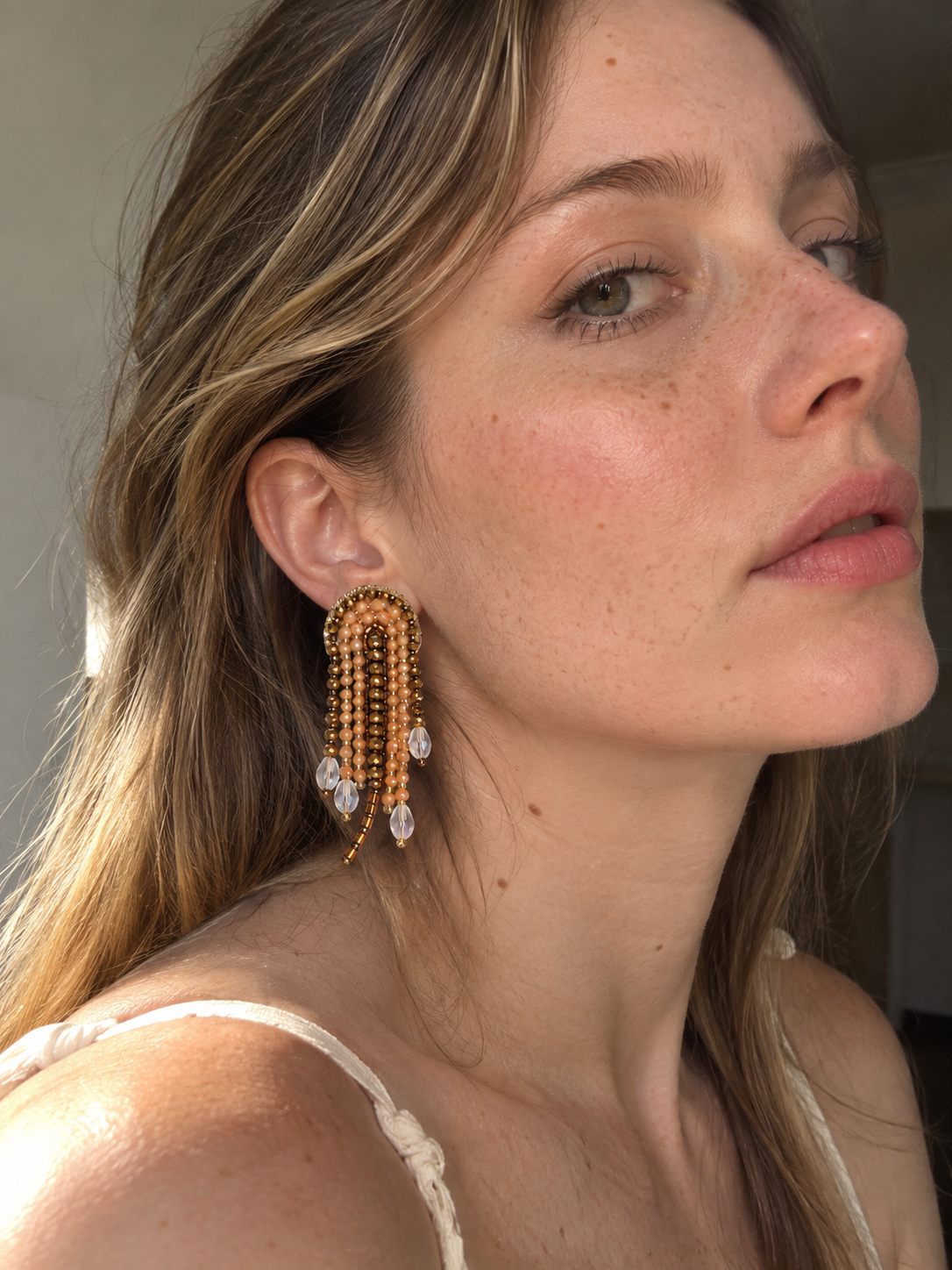 Modelo con un arete Medusa dorado de cuentas y colgantes transparentes en forma de gota.