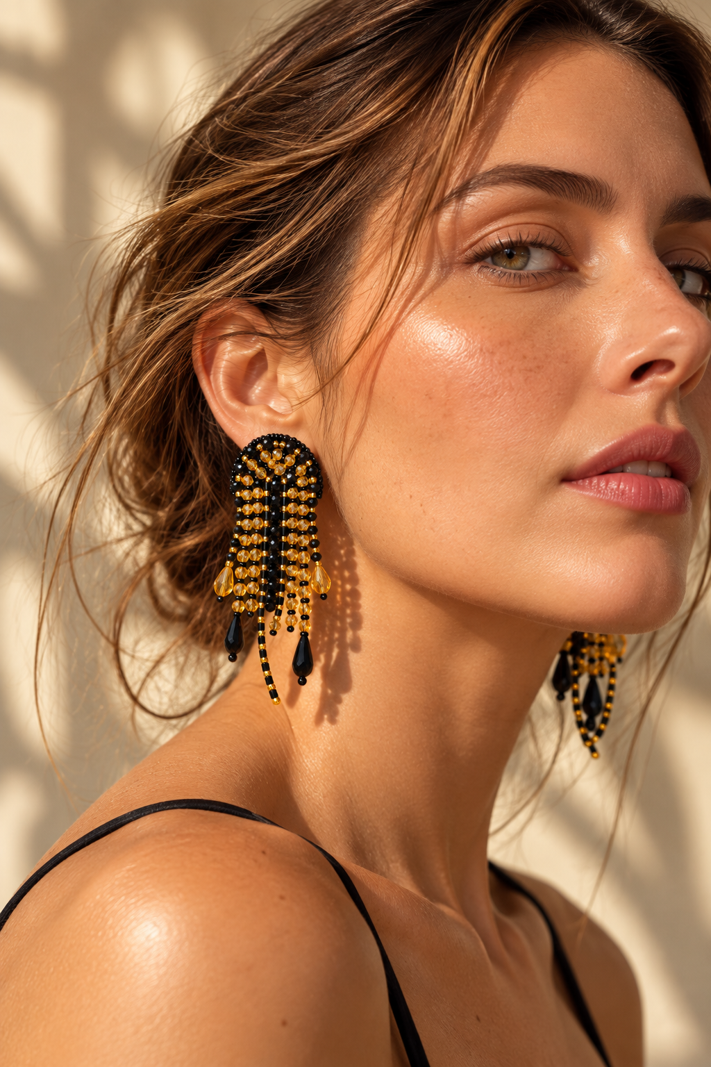 Modelo con aretes Medusa negros y dorados con flecos de cuentas y colgantes en forma de gota.
