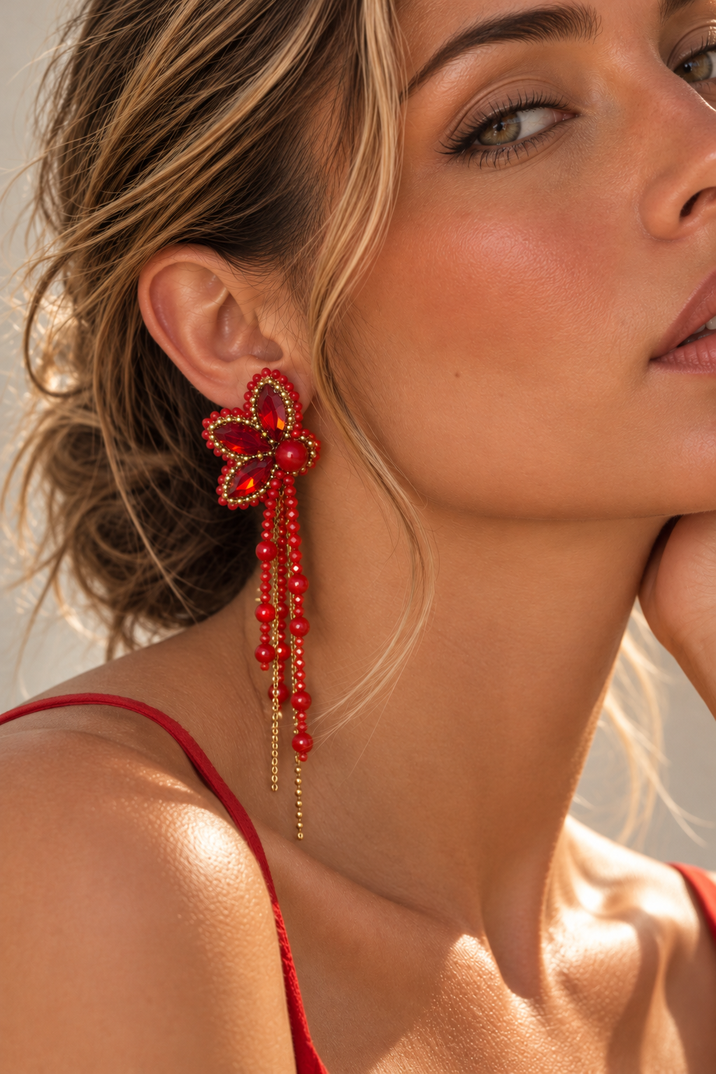 Primer plano de una modelo luciendo un arete Cayena rojo con cristales, cuentas y cadenas doradas.