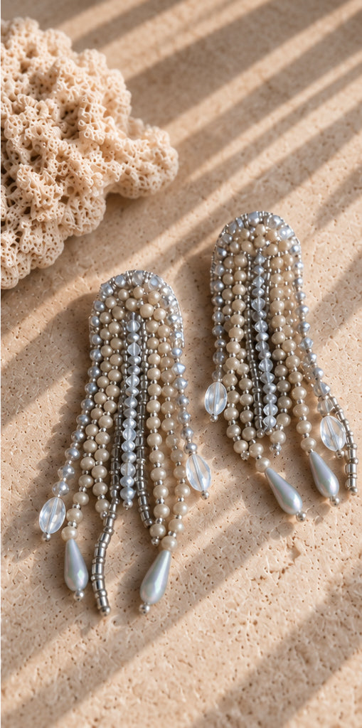 Aretes Medusa plateados con flecos de cuentas y colgantes en forma de gota sobre piedra junto a un coral.